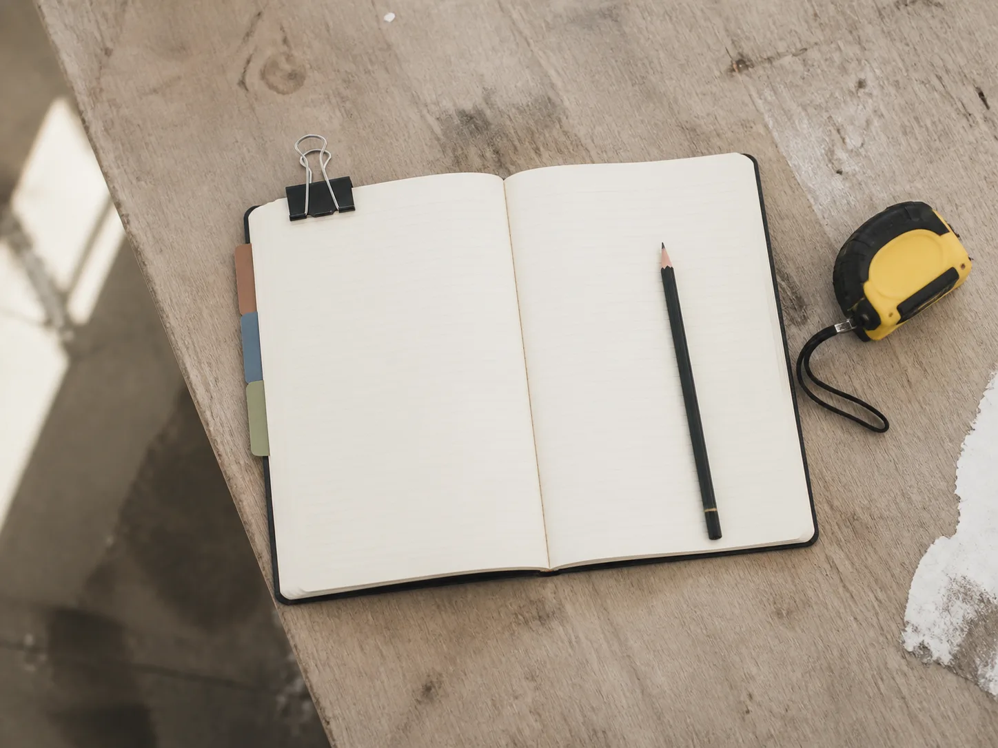 Carnet ouvert, onglets colorés, crayon et mètre sur une table usée